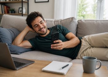 Korepetytor leży na kanapie i sprawdza grafik zajęć na telefonie, zarządzając korepetycjami online w aplikacji dla korepetytorów Reservis