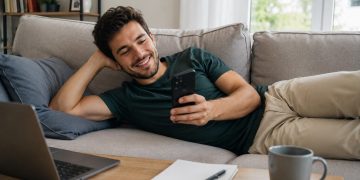 Korepetytor leży na kanapie i sprawdza grafik zajęć na telefonie, zarządzając korepetycjami online w aplikacji dla korepetytorów Reservis